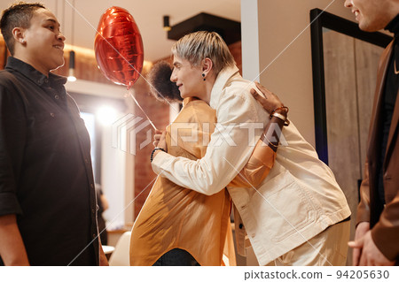 Side view of two young friends in casualwear giving each other hug Side view of two young friends in casualwear giving each other hug 94205630