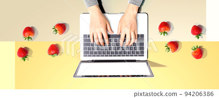 Woman using a laptop computer with fresh strawberries 94206386