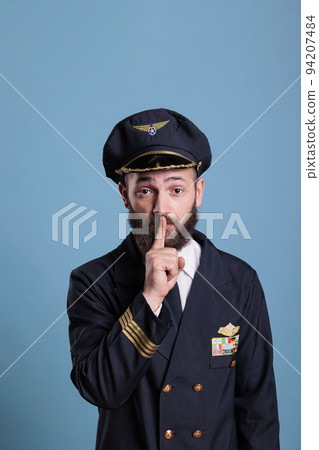 Portrait of captain showing silent gesture, looking at camera with forefinger on lips. Aviation academy plane pilor front view, airforce aviator keeping secret, quiet, silence sign 94207484