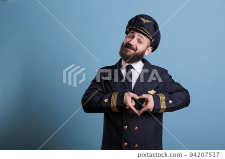 Smiling airplane pilot showing heart shaped love symbol with fingers, conceptual romance gesture. Friendly aircraft captain in uniform expressing affection feelings front view medium shot Smiling airplane pilot showing heart shaped love symbol with fingers, conceptual romance gesture. Friendly aircraft captain in uniform expressing affection feelings front view medium shot 94207517