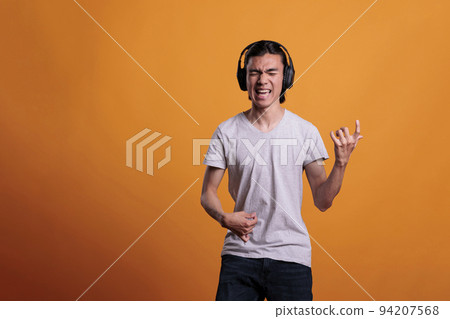 Young asian man in headphones playing virtual guitar, imagining rockstar lifestyle. Musician practicing, teenager using imaginable musical instrument, fun pastime, leisure activity Young asian man in headphones playing virtual guitar, imagining rockstar lifestyle. Musician practicing, teenager using imaginable musical instrument, fun pastime, leisure activity 94207568