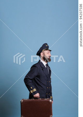 Airplane pilot in professional airline uniform walking with luggage. Smiling aviator with luggage ready for flight, walking in airport, capitan holding suitcase, side view Airplane pilot in professional airline uniform walking with luggage. Smiling aviator with luggage ready for flight, walking in airport, capitan holding suitcase, side view 94207586