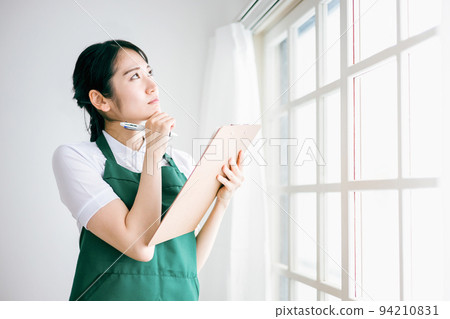 一個穿著圍裙檢查窗戶和窗簾欄杆的女人（擔心） 94210831