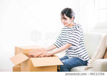 一個女人笑著從紙箱裡拿出衣服 94211708