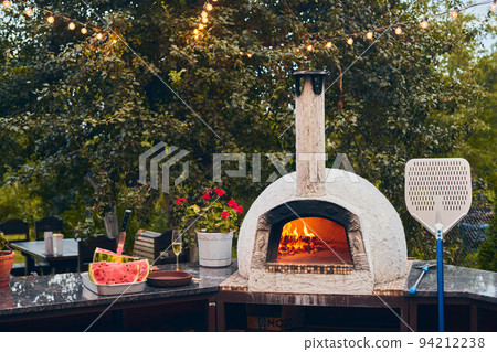 Wood-fired pizza oven with birch logs for kindling. The fire burns and the oven heats up. Front view. Wood-fired pizza oven with birch logs for kindling. The fire burns and the oven heats up. Front view. 94212238