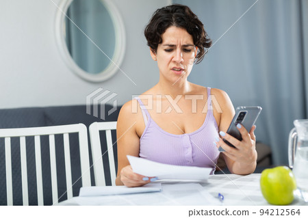 Frustrated brunette woman is unhappy with payment document for utilities Frustrated brunette woman is unhappy with payment document for utilities 94212564