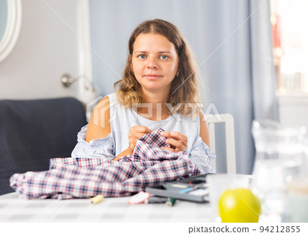 Young woman sewing on button at home Young woman sewing on button at home 94212855