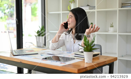 Asian businesswoman or female manager at her office desk, having a business phone call. Asian businesswoman or female manager at her office desk, having a business phone call. 94213929