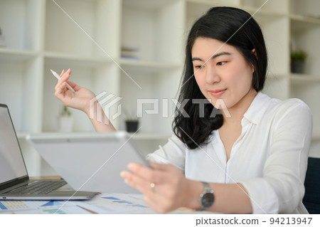 Professional Asian businesswoman is using and looking at a digital tablet at her office desk. Professional Asian businesswoman is using and looking at a digital tablet at her office desk. 94213947