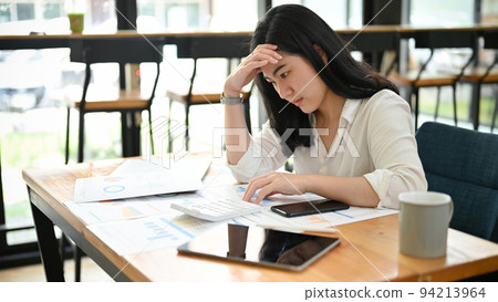 Asian businesswoman, stressed and thoughtful, working remotely from a cafe 94213964