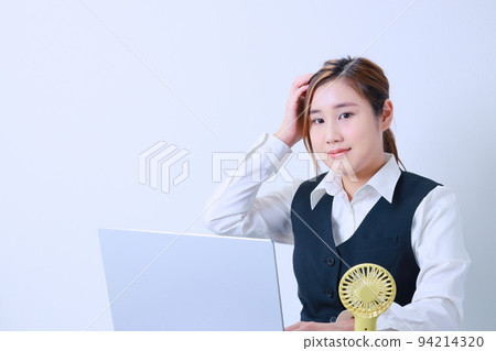 A young office worker holding her head with her right hand while working on a PC 94214320