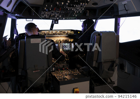 Multiethnic team of pilots using control command to fly plane in aircraft cockpit, pushing power buttons on dashboard. Captain and pilot doing teamwork flying airplane with engine lever. 94215146