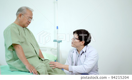 Elder Asian man sitting on the bed and talking to doctor about his physical injuries at his knees, elderly Asian man having a consulting with professional physical therapist or orthopedic doctor. Elder Asian man sitting on the bed and talking to doctor about his physical injuries at his knees, elderly Asian man having a consulting with professional physical therapist or orthopedic doctor. 94215204