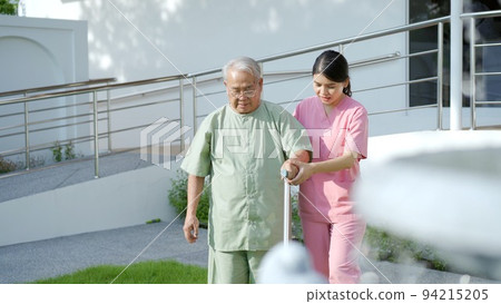 Senior elder Asian man having a physical therapy by walking with cane staff support. Professional caregiver taking an elder Asian old man walking at the park. Senior elder Asian man having a physical therapy by walking with cane staff support. Professional caregiver taking an elder Asian old man walking at the park. 94215205
