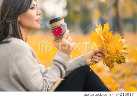 Young mixed race woman drinking coffee in autumn park 94216017