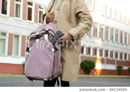 Firearms at school. Schoolgirl with a gun in a backpack on a school background. The girl carries a gun to school. School violence 94216084