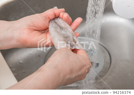 [A middle-aged housewife prepares a squid and washes the inside of its body] 94216374