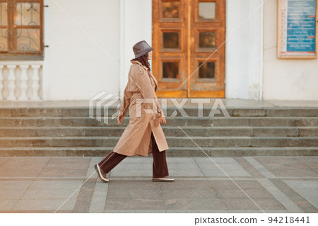 Outdoor fashion portrait of young elegant fashionable brunette woman, model in stylish hat, choker and light raincoat posing at sunset in European city. Outdoor fashion portrait of young elegant fashionable brunette woman, model in stylish hat, choker and light raincoat posing at sunset in European city. 94218441