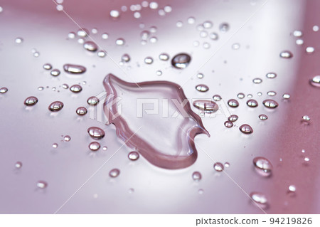A large drop and splashes of micellar water on a pink background. A large drop and splashes of micellar water on a pink background. 94219826