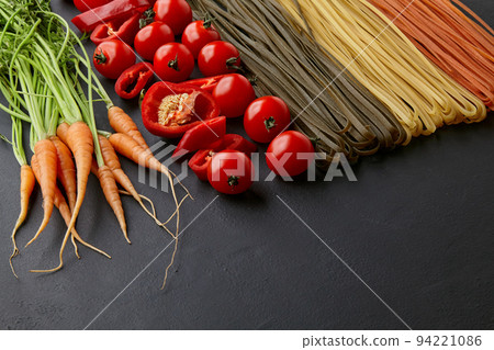 Homemade colorful pasta with natural ingredients on a black concrete table. Noodles with tomatoes, carrots, paprika Homemade colorful pasta with natural ingredients on a black concrete table. Noodles with tomatoes, carrots, paprika 94221086