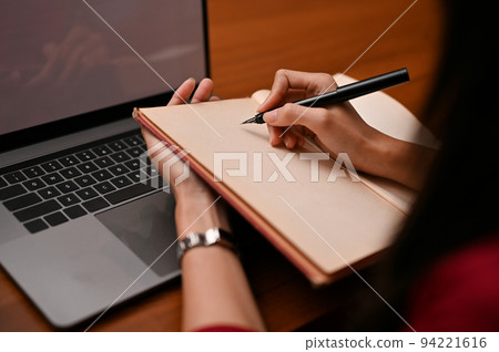 A businesswoman writing or taking notes something on her blank notebook at her office desk. A businesswoman writing or taking notes something on her blank notebook at her office desk. 94221616