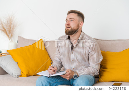 An image concentrated young bearded man sitting in notes on couch at home An image concentrated young bearded man sitting in notes on couch at home 94222158