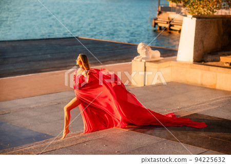 A woman in a long red dress against the backdrop of sunrise, bright golden light of the sun's rays. The concept of femininity, harmony. 94225632