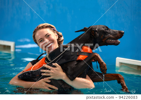 Dog in life jacket swim in the swimming pool with coach. Pet rehabilitation. Recovery training prevention for hydrotherapy. Pet health care 94226083