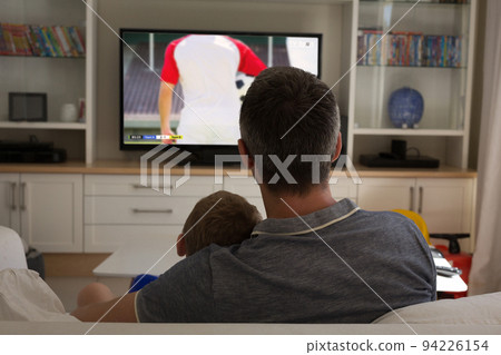 Caucasian father and son watching football match together and sitting on the couch Caucasian father and son watching football match together and sitting on the couch 94226154