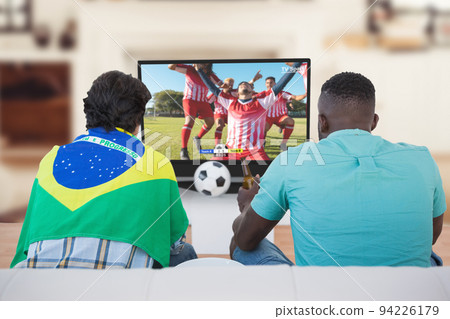 Two diverse friends watching football match together and sitting on the couch 94226179