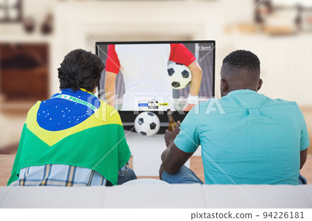 Two diverse friends watching football match together and sitting on the couch Two diverse friends watching football match together and sitting on the couch 94226181