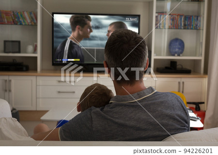 Father and son watching football match siting together on the couch Father and son watching football match siting together on the couch 94226201