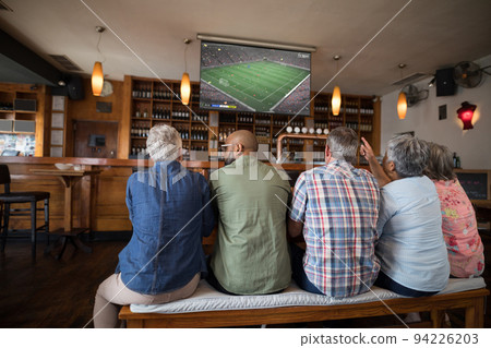 Group of senior people watching football match siting together in bar Group of senior people watching football match siting together in bar 94226203