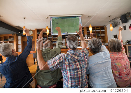 Happy group of senior people watching football match siting together in bar Happy group of senior people watching football match siting together in bar 94226204