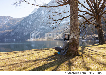 Young man sitting outdoors and enjoying mountains, snow, lake, good weather, blue sky, sun. Beautiful landscape. Time with yourself, dreaming, relaxation, mental health. Tourism, holiday and travel. Young man sitting outdoors and enjoying mountains, snow, lake, good weather, blue sky, sun. Beautiful landscape. Time with yourself, dreaming, relaxation, mental health. Tourism, holiday and travel. 94227059