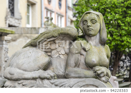 Sphinx sculpture, a fusion of a lion and a woman made from stone on the street of Old Town in Gdansk, Poland. Mysterious woman sphinx statue lies near old building in the park 94228383