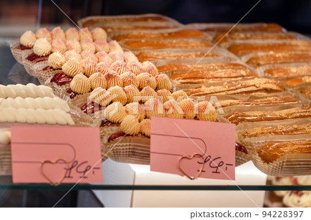Eclairs on the shelf of a pastry shop or cafe. Tasty french sweets on window shop, delicious pastries for coffee. Cakes in pastry shop, variety of desserts with creamy topping on display in bakery 94228397