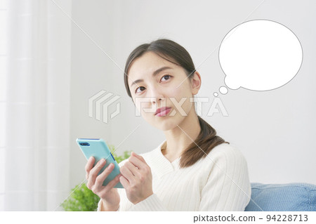 A woman holding a smartphone and thinking in the living room with a speech bubble A woman holding a smartphone and thinking in the living room with a speech bubble 94228713