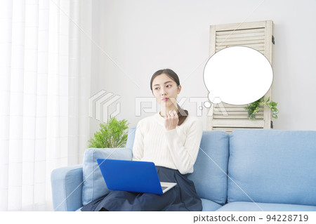A woman thinking while using her laptop in the living room with a speech bubble A woman thinking while using her laptop in the living room with a speech bubble 94228719