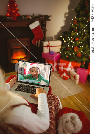 Santa claus making laptop christmas video call with smiling african american boy 94229436