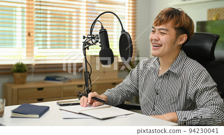 Cheerful Asian man using microphone while streaming audio podcast at home studio. Entertainment, podcasts and technology concept 94230041