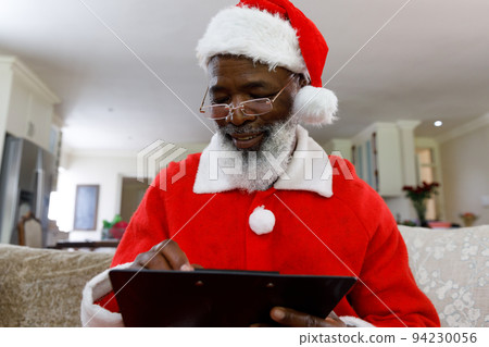 Senior african american man wearing a costume of santa claus and writing on clipboard 94230056