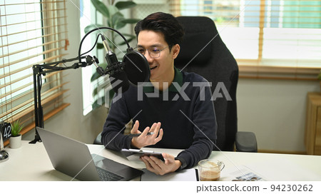 Asian male vlogger using microphone and laptop recording podcast for channel in home studio 94230262