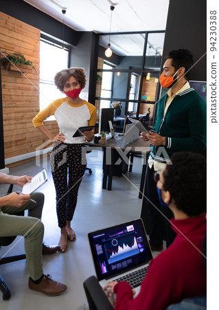 Diverse group of colleagues wearing masks having disussion in creative office Diverse group of colleagues wearing masks having disussion in creative office 94230388