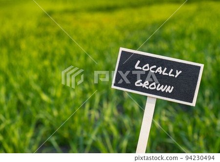 Wooden information label sign with text LOCALLY GROWN against defocused agriculture field message. supporting local farmers Harvest Wooden information label sign with text LOCALLY GROWN against defocused agriculture field message. supporting local farmers Harvest 94230494