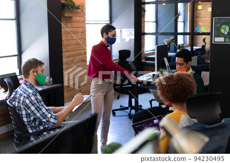 Diverse group of colleagues wearing masks having casual meeting in creative office Diverse group of colleagues wearing masks having casual meeting in creative office 94230495