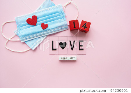 Valentine's Day celebration concept. Wooden cubes 14 February on a pink background. The heart lies on medical masks, the fight against coronavirus. 94230901