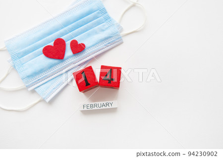 Valentine's Day celebration concept. Wooden cubes on February 14th. The heart lies on medical masks, the fight against coronavirus. 94230902