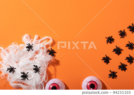 Multiple spider toys forming a spider web and scary eyes toys with copy space on orange background Multiple spider toys forming a spider web and scary eyes toys with copy space on orange background 94231103