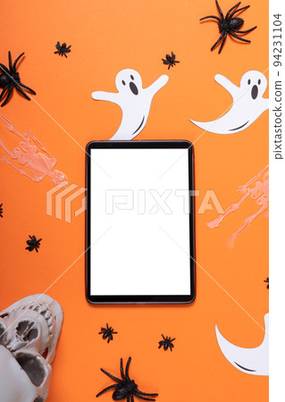 Digital tablet with copy space and multiple halloween concept toys against orange background 94231104